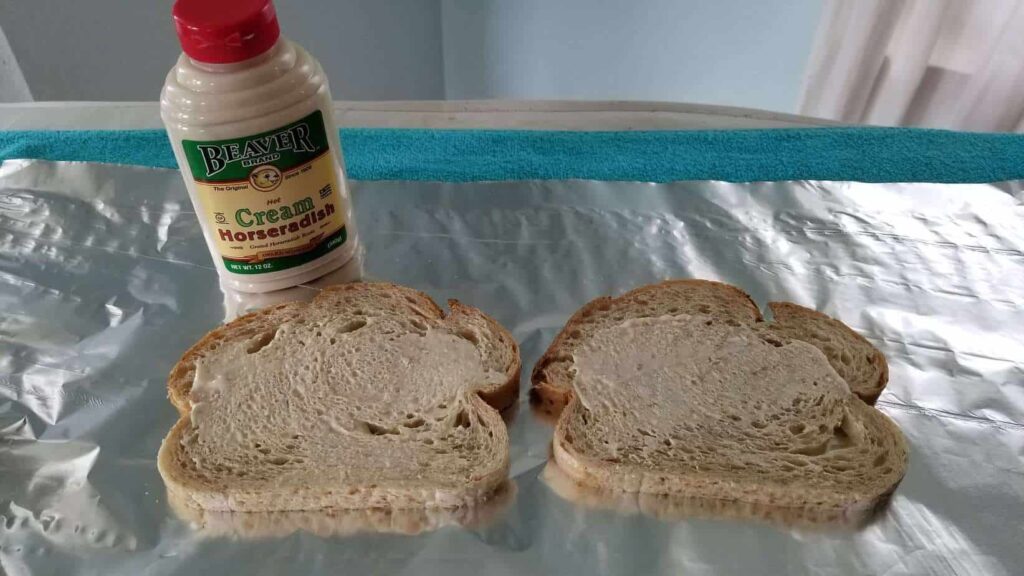 Two slices of sourdough bread on foil, with a bottle of horseradish cream