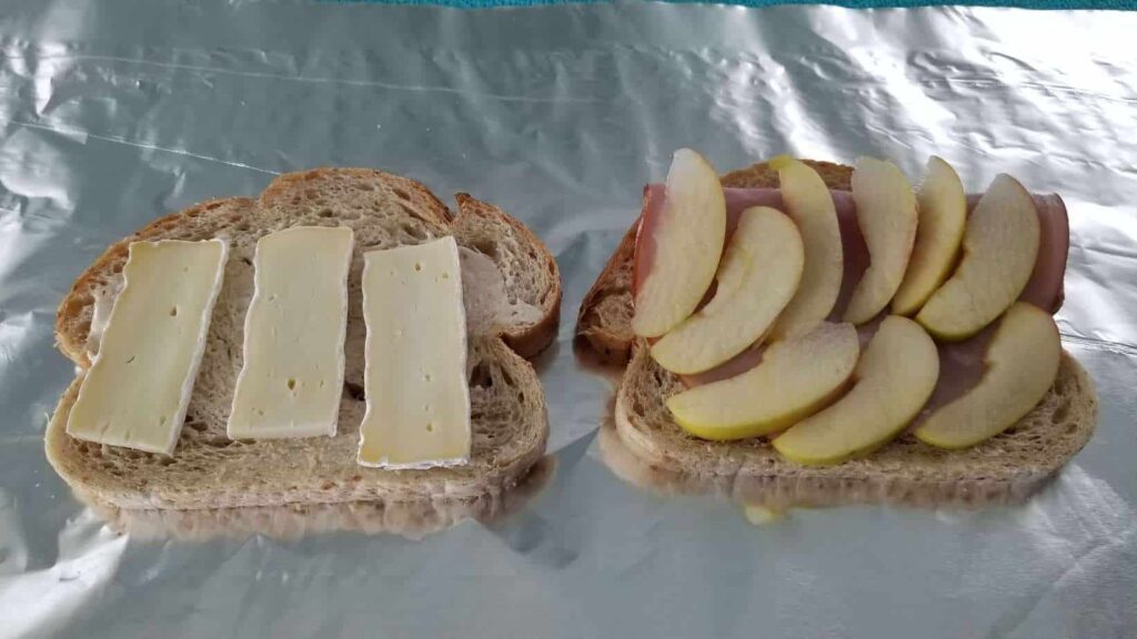 Two slices of bread with brie on one side and sliced apples on the other, on a background of foil