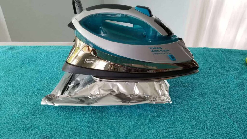 A turquoise iron sitting on top of a foil packet, inside is a ham and brie sandwich