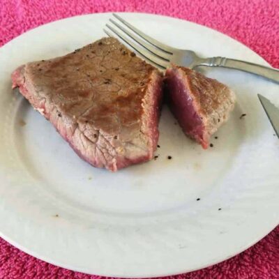 A steak cooked to medium rare on a white plate and fork