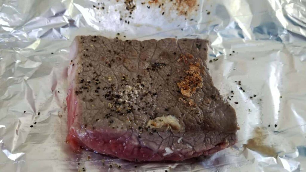A seared steak, cooked on one side and sitting on a piece of foil