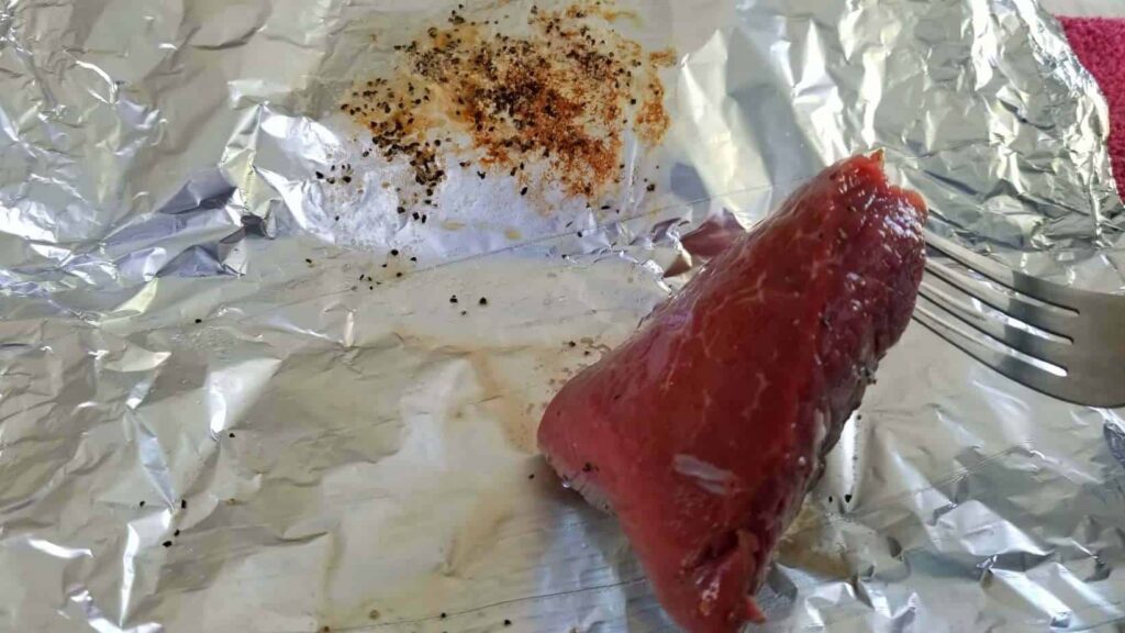 A piece of steak being flipped over on foil