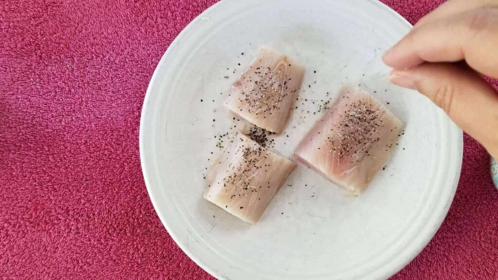 Three pieces of raw tuna, sprinkled with salt and pepper on a white plate 
