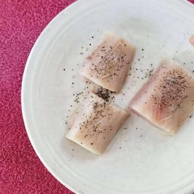 Three pieces of raw tuna, sprinkled with salt and pepper on a white plate