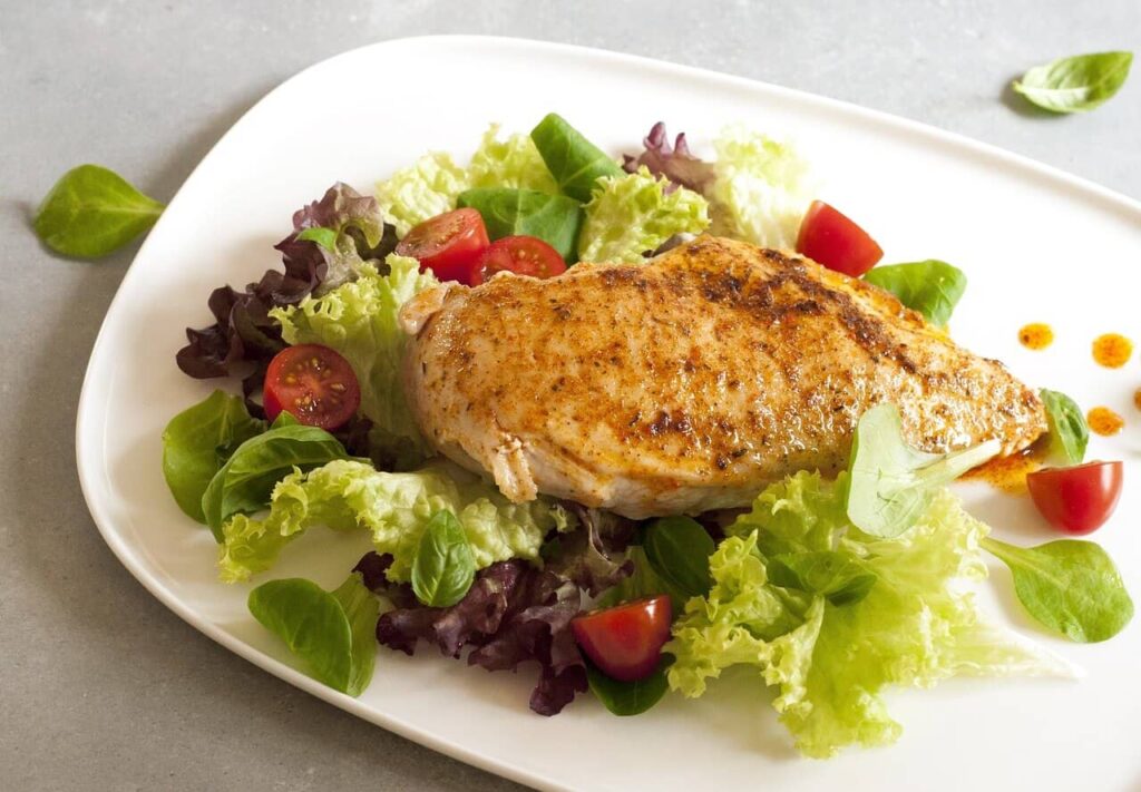 Grilled chicken on a green salad, served on a white plate.