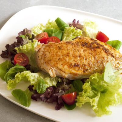 Grilled chicken on a green salad, served on a white plate.
