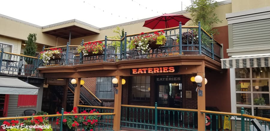 Sun deck at 5th Street Market. Eugene, OR. Red geraniums fill pots around the deck. Bright red sun umbrellas. 