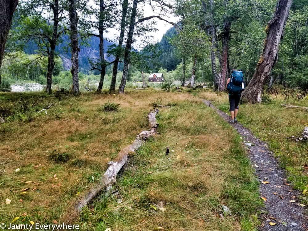 backpacker on the trail, ranger cabin in the distance 