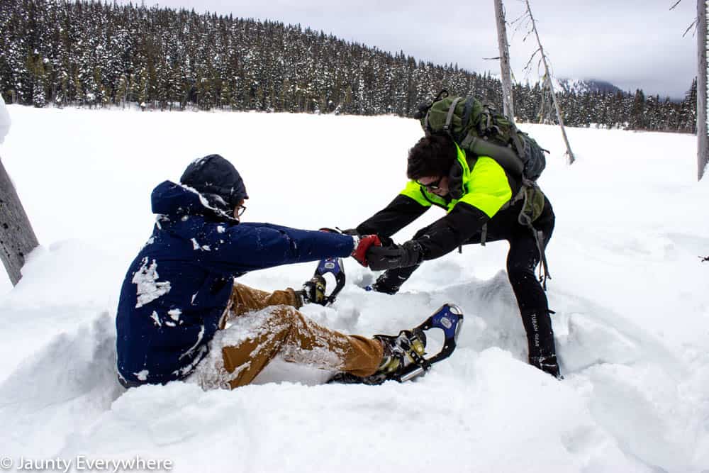 Man sitting in snow getting helped up by a second man.