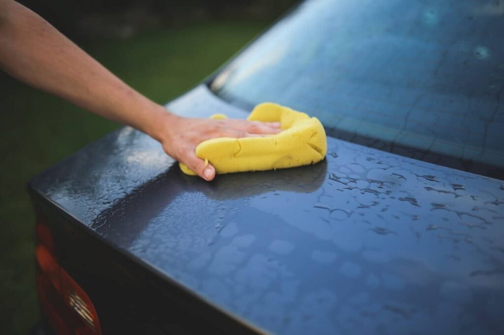 Hand holding a yellow sponge washing a car