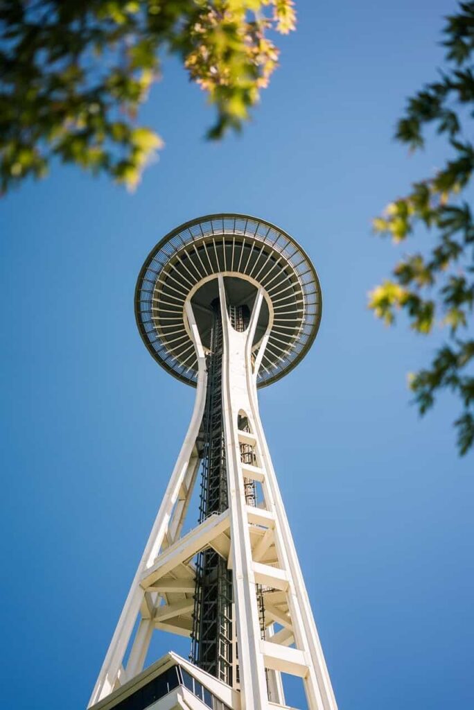 Seattle Space Needle against a pure blue sky, with tree leaves along the edges of the frame