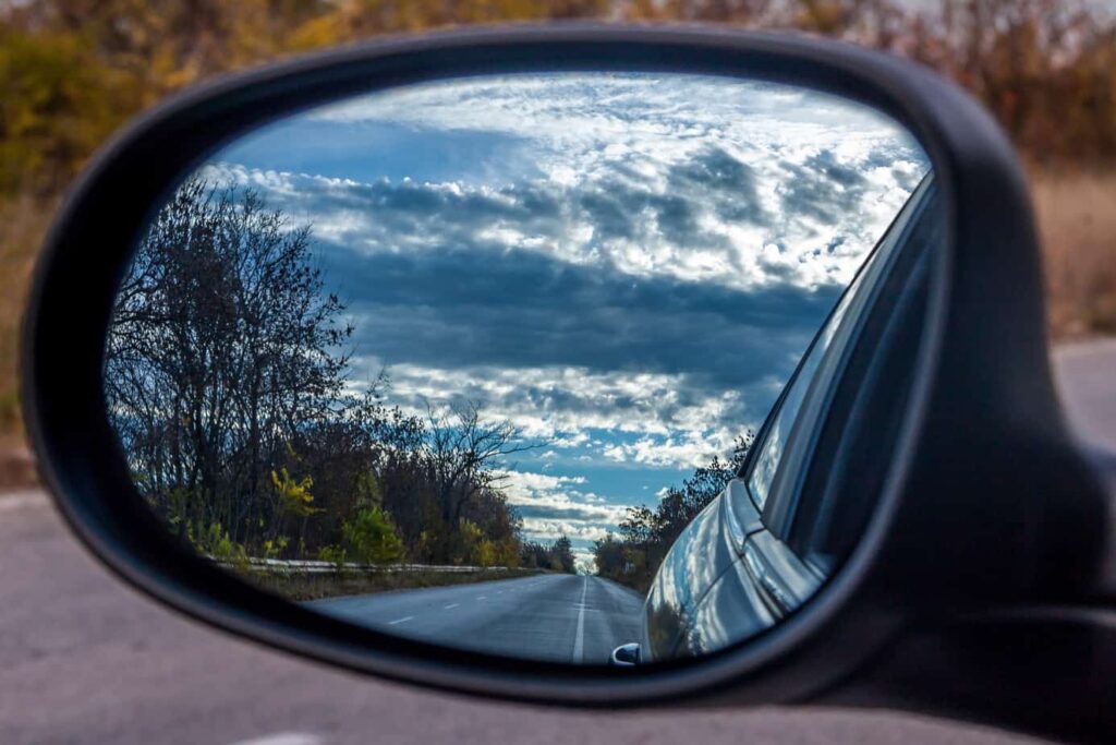 Rear view mirror with a view of the sky and road.