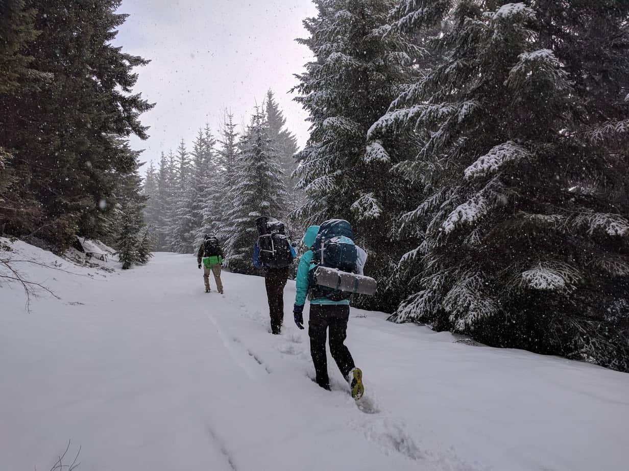 Backpacking in a snowstorm. Jordan and Brittany Stanton and Andrew Bywater walking in snow in a forest. Backpacking tips for beginners.