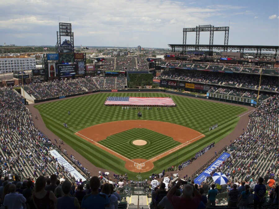 an aerial view of a baseball stadium, filled with fans, the american flag is displayed on the field during the national anthem