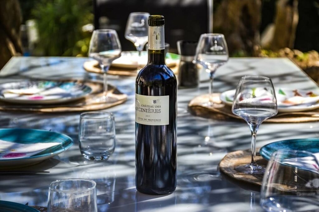 a table under the trees, set for lunch with placemats, colorful plates, glasses and a bottle of wine