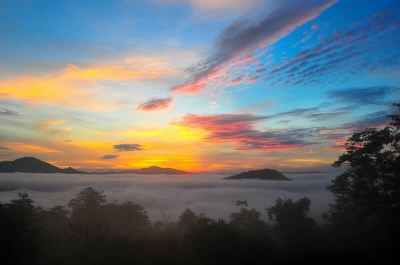 A sunrise over the peak of mountains. Clouds cover the valley. 