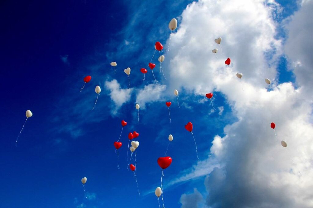 red and white heart balloons floating in a blue sky