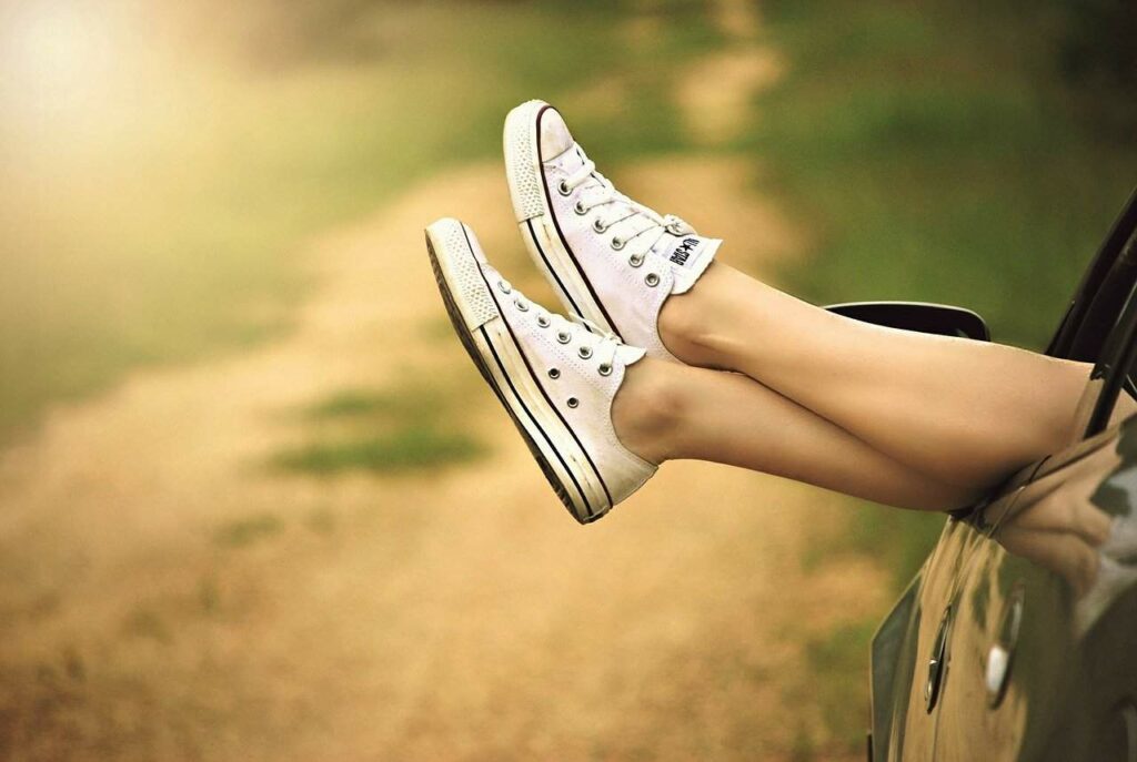 woman wearing white converse shoes with her feet hanging out a car window