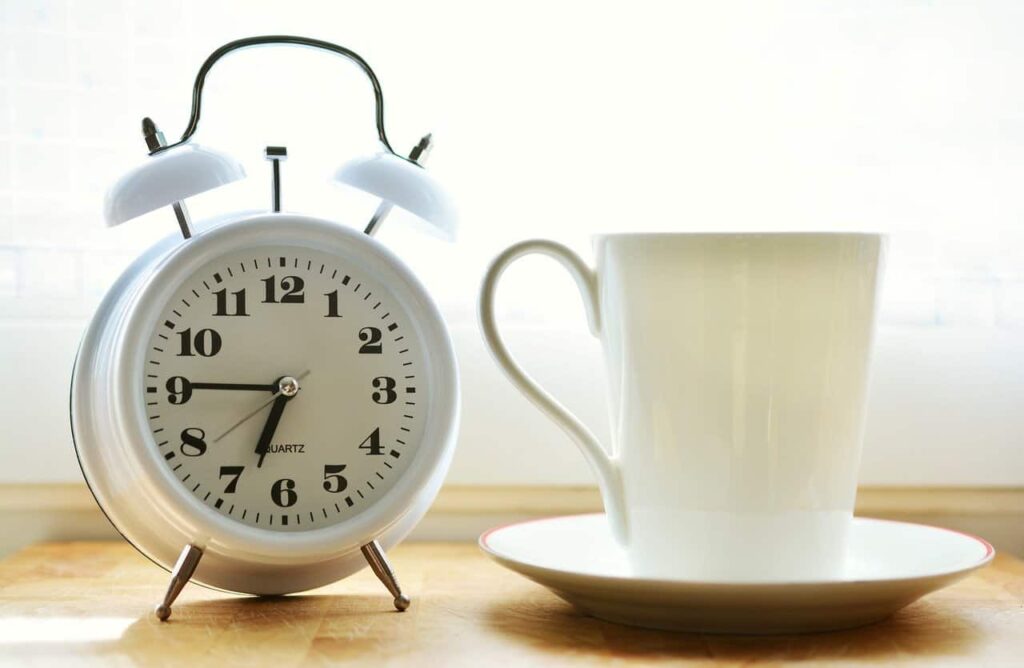white alarm clock next to a white coffee cup on a saucer