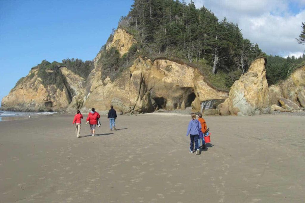 People walking on the sand toward a rock outcropping on Hug Point Beach, Oregon.