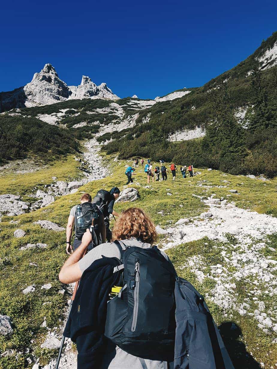 single file row of hikers make their way up an alpine trail