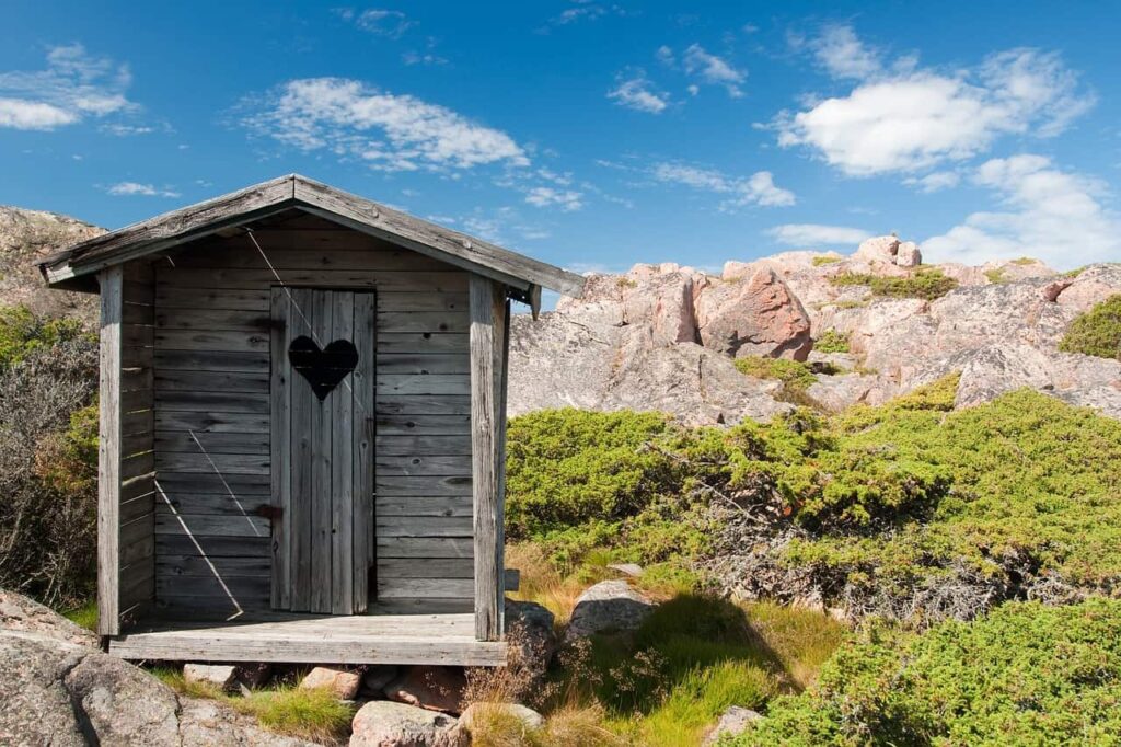 wooden outhouse with a heart shaped cut out in the door, set on a rocky outcropping