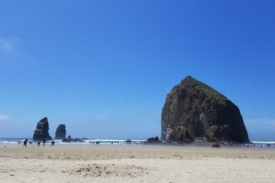 Haystack Rock at Cannon Beach, Oregon, people wading in the tidepools in the distance