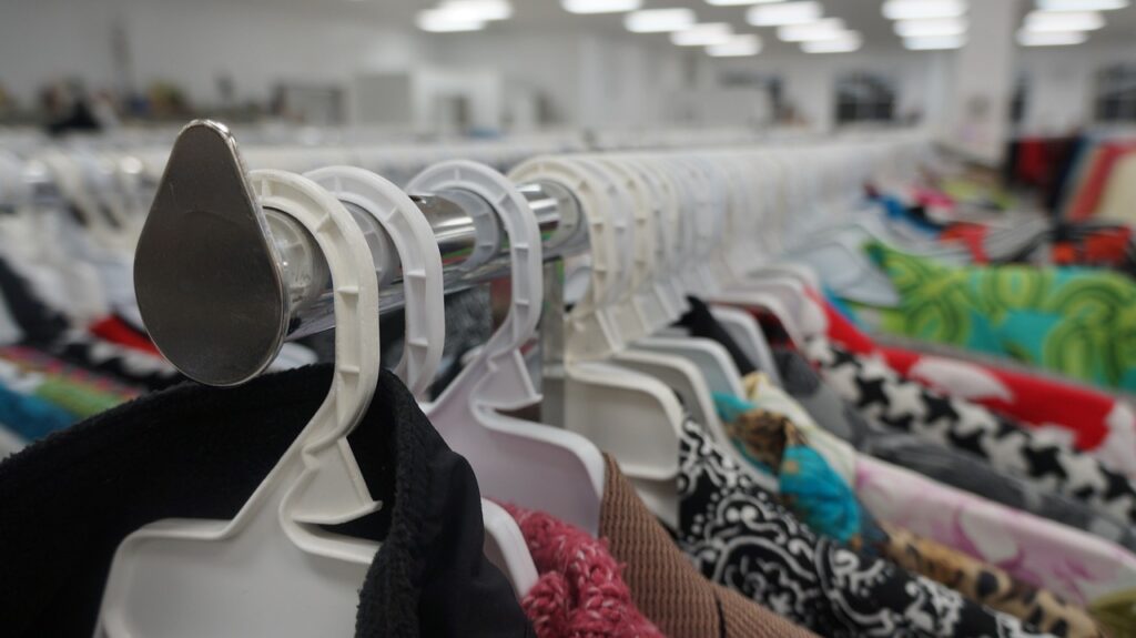 rows of white plastic hangers in a thrift store, the top of colorful blouses fade into the distance 