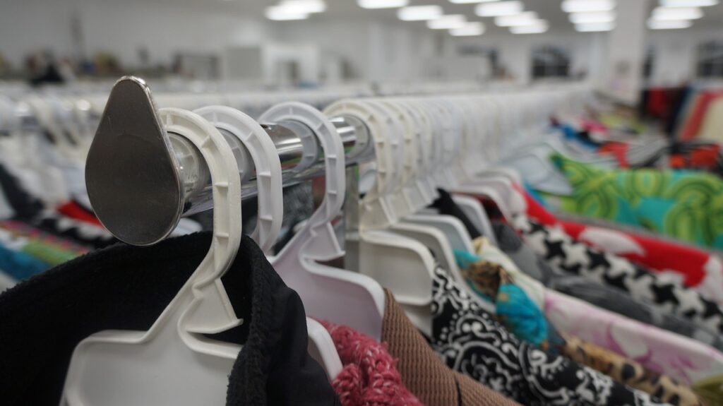 rows of white plastic hangers in a thrift store, the top of colorful blouses fade into the distance