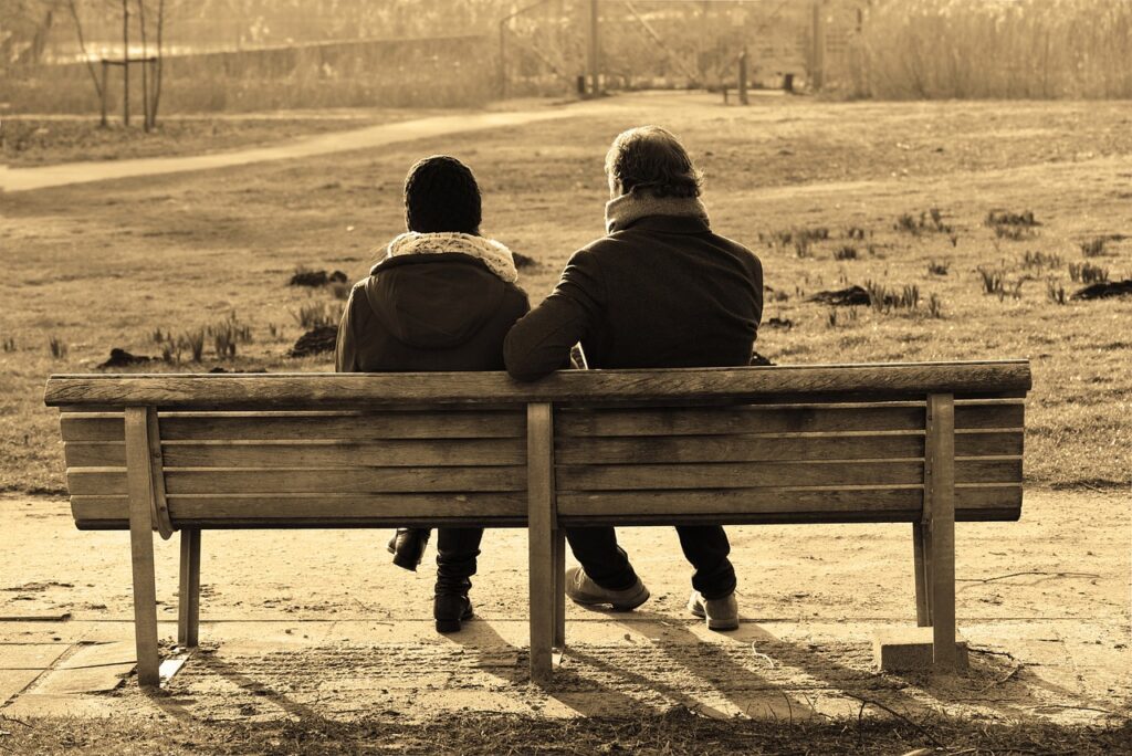 couple sitting on a park bench with their backs to the camera, photo is sepia toned