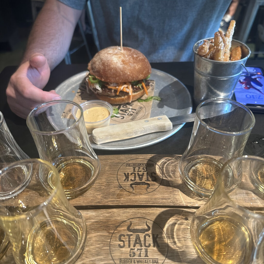 whiskey glasses on a taster tray and a burger on an aluminum plate at Stack 571 in Vancouver, WA