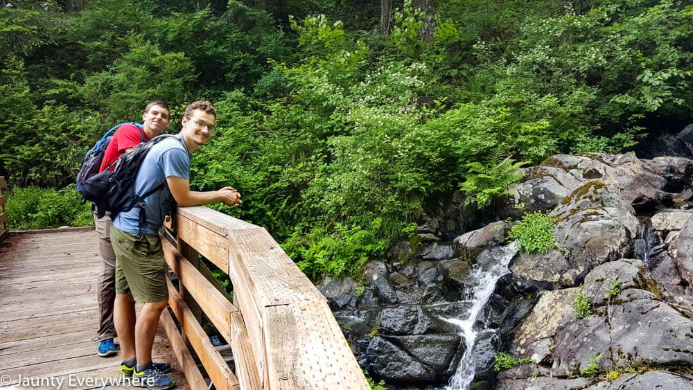 A man and teenager leaning on a bridge on the Silver Star trail a small waterfall is flowing down rocks in the background