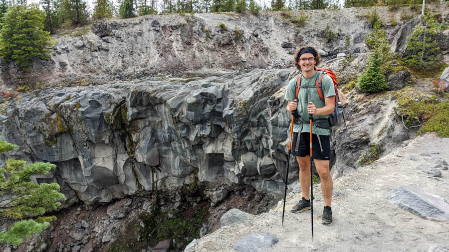 Man stands on a sandy trail on the edge of a cliff holding hiking poles.